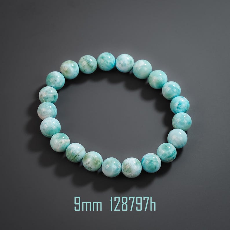 May include: A circular bracelet composed of smooth, round, light blue and white marbled beads. The beads measure 9mm in diameter as indicated by the text 9mm 128797h printed below the bracelet. The stones feature a polished finish.