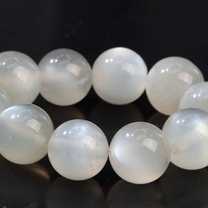 May include: A strand of white moonstone beads. The beads are round and have a smooth, polished finish. The beads are strung on a clear elastic cord.