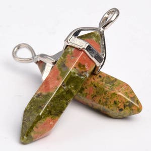 May include: Two green, red, and brown gemstone pendants with silver metal settings. The pendants are shaped like points and are attached to a silver loop.