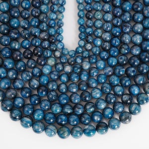 May include: Close-up of a collection of blue gemstone beads. The beads vary in size and are a deep, mottled blue color with lighter blue and white veining. The beads are arranged in strands, suggesting they are for jewelry making.