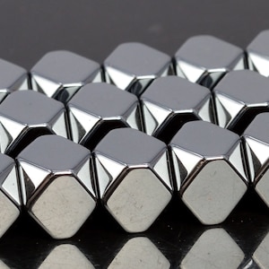 Może przedstawiać: Zbliżenie na sznur srebrzystych, fasetowanych, sześciokątnych koralików. Koraliki są ułożone w przesunięty wzór, tworząc geometryczny wzór.