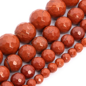 May include: A strand of red gemstone beads with a faceted finish. The beads are arranged in a graduated size, with the largest beads at the top and the smallest beads at the bottom.