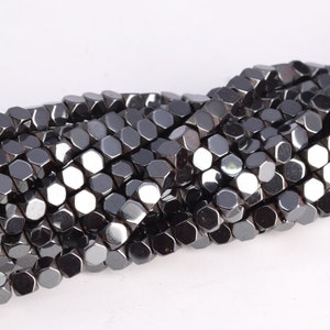 May include: A strand of black hematite beads, each bead is faceted and shaped like a hexagon. The beads are arranged in a loose, flowing pattern.
