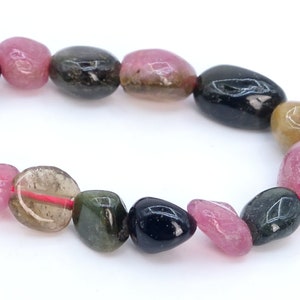 May include: A strand of multi-colored gemstone beads. The beads are oval shaped and have a smooth, polished finish. The colors of the beads are pink, green, black, and brown.