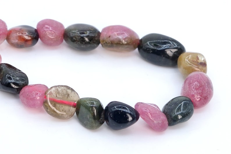 May include: A strand of multi-colored gemstone beads. The beads are oval shaped and have a smooth, polished finish. The colors of the beads are pink, green, black, and brown.