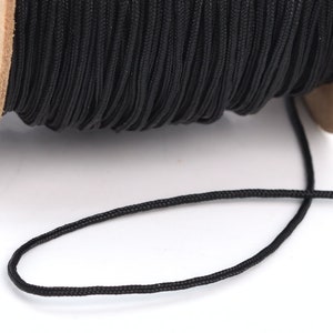 May include: A spool of black cord, with a length of cord extending from the spool.