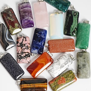 May include: A collection of rectangular stone pendants featuring various colors and patterns, including purple, pink, white, blue, green, brown, and black. Each pendant is fitted with a silver-toned metal bail at the top for attachment.