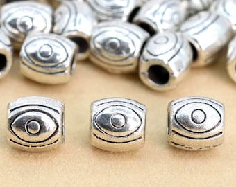 Peut inclure: Perles en métal argenté avec un motif œil. Les perles sont de forme ovale et ont une surface texturée.