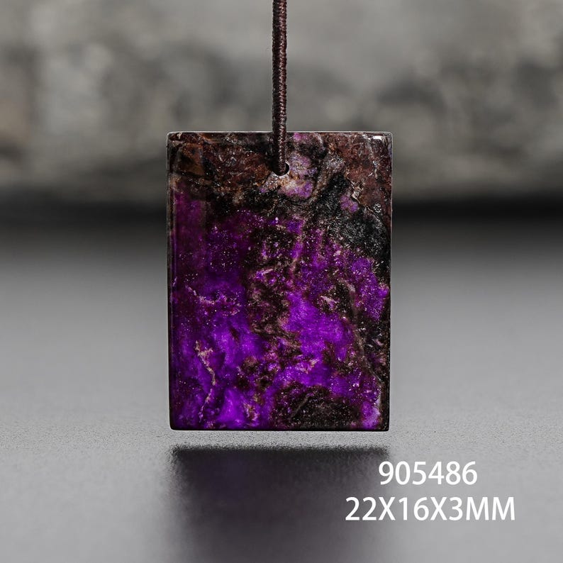 Op de afbeelding: Een rechthoekige hanger met een levendig paars en bruin gemarmerd patroon, opgehangen aan een donkerbruin koord. Afmetingen: 22mm x 16mm x 3mm. Artikelnummer 905486.