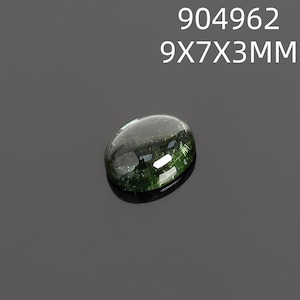 May include: A polished, oval-shaped gemstone with a dark green hue and internal inclusions. The gem measures 9x7x3mm and is set against a dark gray background. The text "904962 9X7X3MM" is displayed above the gem.