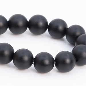 May include: A strand of black matte round beads. The beads are smooth and uniform in size.