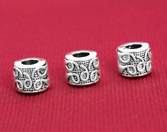 Pode incluir: Três contas de metal prateado com um design intrincado e em espiral. As contas são redondas e têm um furo no centro.