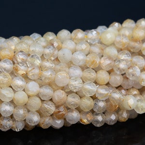 May include: A strand of faceted golden rutilated quartz beads. The beads are translucent and have a light yellow color with gold inclusions.