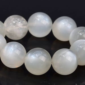 May include: A strand of white moonstone beads, each bead is round and smooth with a subtle iridescent sheen.