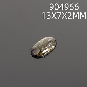 May include: An oval-shaped, translucent gemstone with a smoky, brownish-yellow hue. The gem measures 13mm x 7mm x 2mm and is set against a dark gray background. The text "904966 13X7X2MM" is displayed above the gem.
