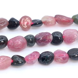 May include: A strand of multi-colored gemstone beads. The beads are a mix of pink, black, and green, and are tumbled into a smooth, oval shape.