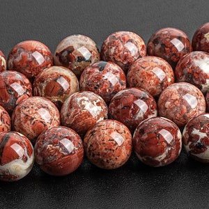 May include: A collection of red and white jasper beads, each with a unique pattern of swirling colours. The beads are smooth and polished, and they have a natural, earthy look.