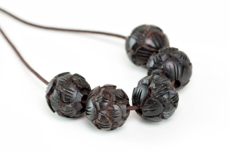 Puede incluir: Un collar de madera marr&oacute;n oscuro con cuentas talladas. Las cuentas son redondas y tienen un patr&oacute;n floral. El collar est&aacute; encordado en un cord&oacute;n marr&oacute;n.