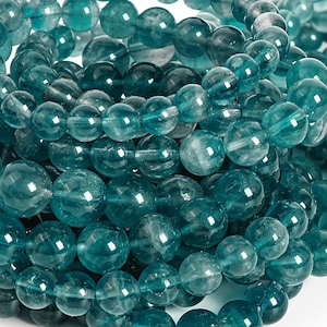 May include: Close-up of a collection of teal-colored, round beads. The beads vary in size and have a translucent quality, with visible internal patterns. The beads are strung together, creating a textured and layered appearance. Ideal for jewelry making.