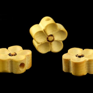 May include: Three wooden flower-shaped beads in a light yellow color. The beads have a hole in the center for stringing.