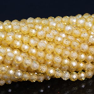 Puede incluir: Primer plano de un hilo de cuentas de cristal amarillo facetadas. Las cuentas son redondas con m&uacute;ltiples facetas, creando un efecto brillante. Las cuentas son de un color amarillo claro y c&aacute;lido, y est&aacute;n ensartadas. Ideal para la fabricaci&oacute;n de joyas.