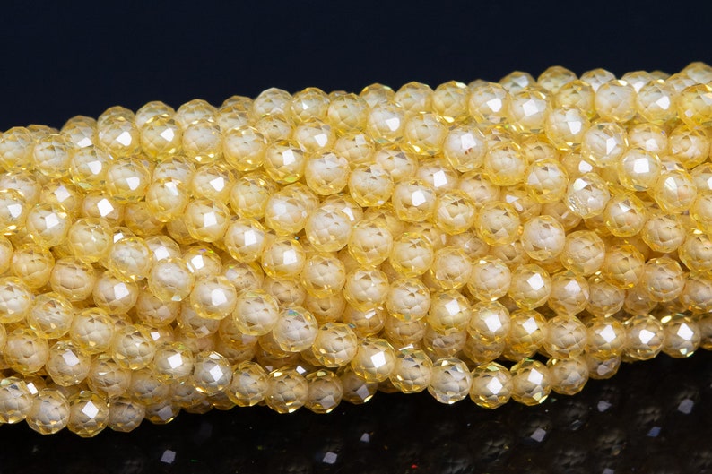 Puede incluir: Primer plano de un hilo de cuentas de cristal amarillo facetadas. Las cuentas son redondas con m&uacute;ltiples facetas, creando un efecto brillante. Las cuentas son de un color amarillo claro y c&aacute;lido, y est&aacute;n ensartadas. Ideal para la fabricaci&oacute;n de joyas.