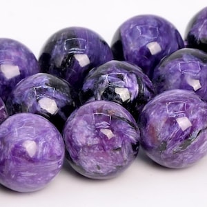 Puede incluir: Una hebra de cuentas redondas de piedras preciosas de color púrpura y negro. Las cuentas tienen un patrón de remolino y mármol.