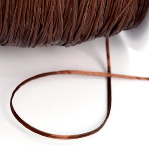 Può includere: Un rocchetto di cordoncino cerato marrone, con un pezzo di cordoncino svolto e che giace su una superficie bianca.