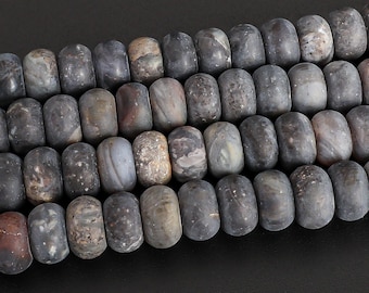 May include: Close-up of a strand of gray and brown gemstone beads. The beads are cylindrical with rounded edges and have a mottled appearance. The beads are strung together, creating a textured and natural look, perfect for jewelry making.