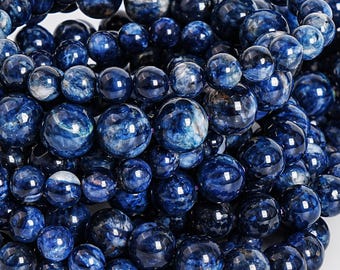 May include: Close-up of a collection of deep blue sodalite gemstone beads. The beads vary in size and have a marbled appearance with white and lighter blue inclusions. The beads are strung together, suggesting they are for jewelry making.