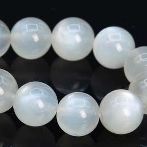 May include: A strand of white moonstone beads, each bead is round and smooth. The beads are strung together on a clear elastic cord.