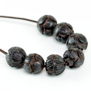 May include: A necklace made of dark brown wooden beads with intricate carvings. The beads are strung on a brown cord.