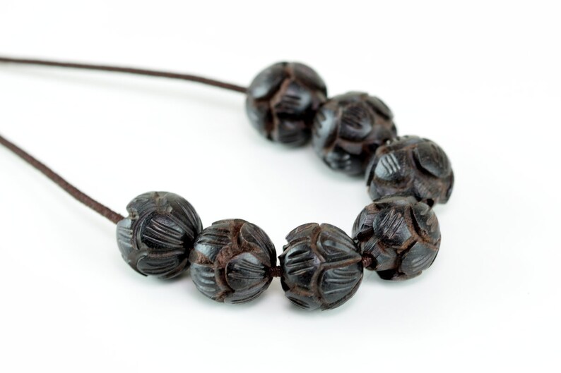 May include: A necklace made of dark brown wooden beads with intricate carvings. The beads are strung on a brown cord.