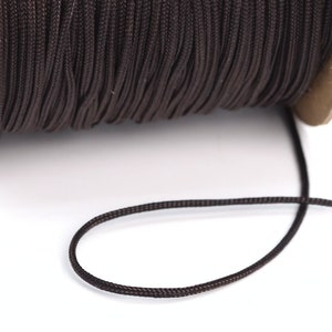 Puede incluir: Una bobina de cordón encerado marrón, con un trozo de cordón que se extiende desde la bobina.