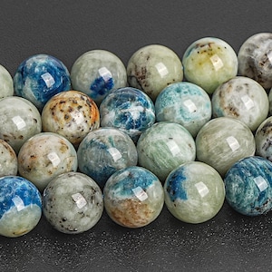 May include: Close-up of a collection of round gemstone beads. The beads are a mix of colors, including blue, green, tan, and white. Each bead has a unique pattern and glossy finish, perfect for jewelry making.