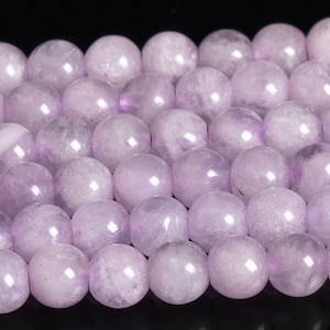 May include: A strand of pale lavender round beads. The beads are smooth and have a slightly translucent appearance.