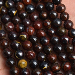 May include: A strand of round, dark brown and red gemstone beads with gold flecks. The beads are approximately 8mm in diameter.