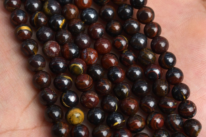 May include: A strand of round, dark brown and red gemstone beads with gold flecks. The beads are approximately 8mm in diameter.