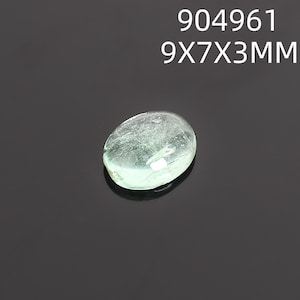 May include: A translucent, oval-shaped gemstone with a pale green hue. The gem measures 9x7x3mm and is set against a dark background. The text "904961 9X7X3MM" is displayed above the gem.
