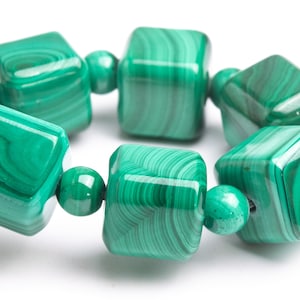 Puede incluir: Un brazalete de malaquita verde con cuentas cuadradas. El brazalete está hecho de piedras naturales y tiene un acabado pulido.