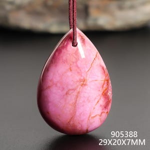 May include: A teardrop-shaped pendant with a pink and red marbled pattern, suspended by a maroon cord. The pendant measures 29mm x 20mm x 7mm. The surface is polished and smooth, with natural veining.