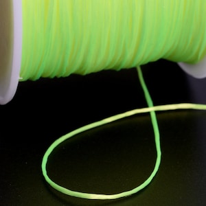 May include: A spool of bright green glow-in-the-dark string. The string is wound around a white spool and a length of string is hanging down.