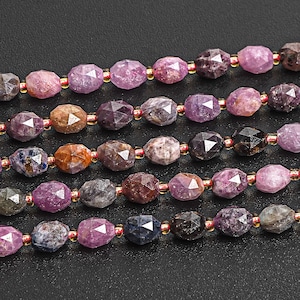 May include: A strand of gemstone beads in various shades of pink, purple, and black. The beads are faceted and have a slightly irregular shape.