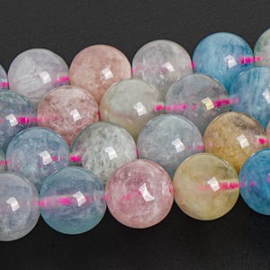 Könnte beinhalten: Eine Reihe runder, mehrfarbiger Edelsteinperlen. Die Perlen sind eine Mischung aus hellblau, rosa und gelb mit einem durchscheinenden, glasartigen Finish.