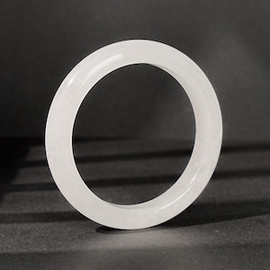 May include: A smooth, circular bangle bracelet crafted from translucent white stone. The piece features a polished, glossy finish with subtle internal cloud-like textures visible throughout the material, creating a clean and uniform appearance.