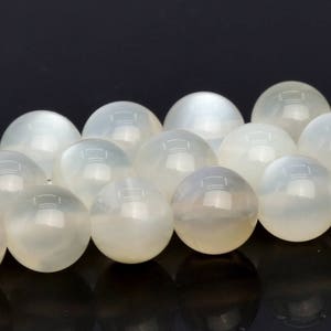 May include: A strand of white moonstone beads. The beads are round and smooth, with a subtle iridescent sheen.