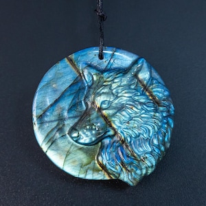 Può includere: Un ciondolo rotondo in labradorite blu con un design a testa di lupo scolpito. Il ciondolo è su un cordoncino nero.