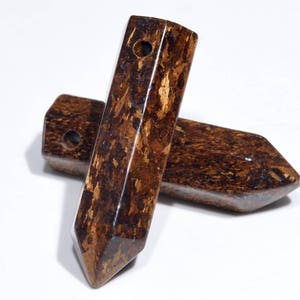 May include: Two brown and gold gemstone points with a hole drilled through the top. The points are made of a natural stone with a unique pattern.