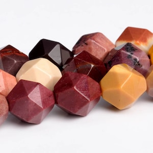 May include: A collection of faceted gemstone beads in various colors, including shades of red, yellow, cream, and brown. The beads have a geometric shape and are arranged against a white background.