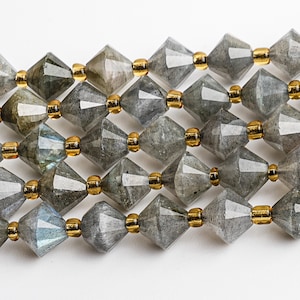 Puede incluir: Una hebra de cuentas de piedras preciosas facetadas en un esquema de colores gris y dorado. Las cuentas son facetadas y tienen forma de diamante. Las cuentas están enhebradas en un alambre dorado.